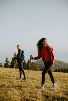 Smiling couple walking with backpacks over green hills photo