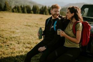 Young couple relaxing by a terrain vehicle hood at countryside photo