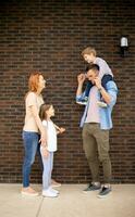 Family with a mother, father, son and daughter standing by the wall of brick house photo