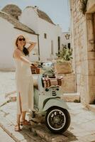 un joven mujer en un blanco vestir y un blanco sombrero durante turista visitar en alberobello, Italia foto