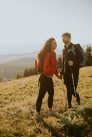 Smiling couple walking with backpacks over green hills photo