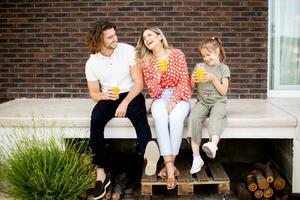 Family with a mother, father and daughter sitting outside on the steps of a front porch of a brick house photo