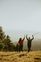 Smiling couple walking with backpacks over green hills photo