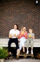 Family with a mother, father and daughter sitting outside on the steps of a front porch of a brick house photo