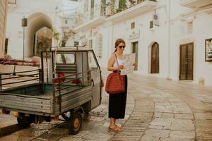 hembra turista con papel ciudad mapa en estrecho calles de ostuni, Italia foto