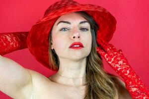 portrait of cute young woman wearing hat and red gloves on red background photo