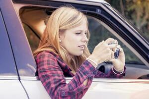 young blond girl takes a photo from a car