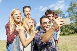 group of smiling friends taking selfie with smartphone photo