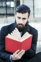 young hipster reading a book sitting outdoors photo