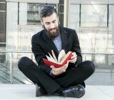 young hipster reading a book sitting outdoors photo
