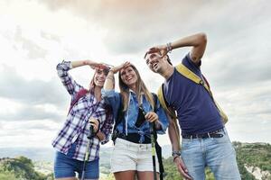 grupo de joven adultos mira a el horizonte durante excursionismo foto