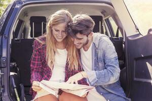 young lovers looking map sitting in the trunk of car photo