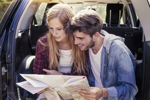 joven amantes mirando mapa sentado en el maletero de coche foto