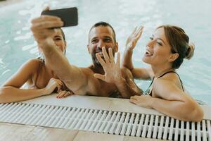joven personas relajante en el interior nadando piscina y tomando selfie con móvil teléfono foto