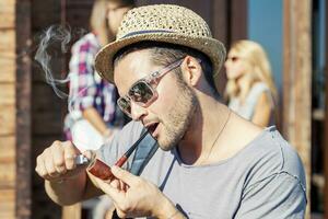 young hiker lights his pipe in front of the hut photo