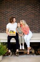 Family with a mother, father and daughter sitting outside on the steps of a front porch of a brick house photo