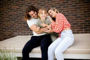 Family with a mother, father and daughter sitting outside on the steps of a front porch of a brick house photo