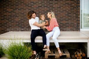 Family with a mother, father and daughter sitting outside on the steps of a front porch of a brick house photo