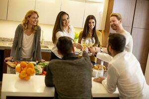 Group of young people preparing meal, drinking white wine and having a good time photo