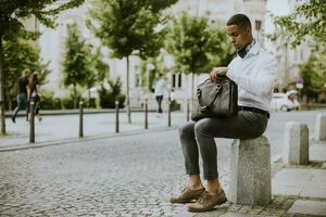 Young African American businessman using a mobile phone while waitng for a taxi on a street photo