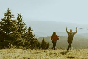 Smiling couple walking with backpacks over green hills photo