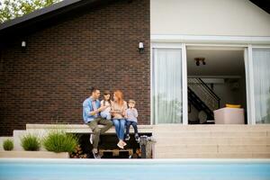 Family with a mother, father, son and daughter sitting outside on steps by the swimming pool and eating strawberries photo