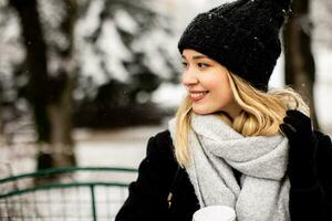 Young woman n warm clothes enjoying in snow with takeaway coffee cup photo