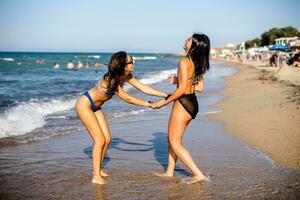 dos bonito joven mujer teniendo divertido en el playa foto