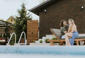 Young couple relaxing by the swimming pool in the house backyard photo