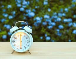 white vintage alarm clock showing 6 o clock on the table in the garden with purple flowers background. photo