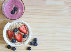 flat lay of  breakfast with a  glass of blueberry smoothie and oat or granola in white bowl, fresh blueberries, strawberries on wooden table. Healthy breakfast concept. photo