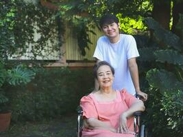 Asian senior woman sitting on wheelchair with her son in the garden. photo