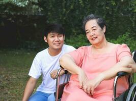 Asian senior woman sitting on wheelchair with her son in the garden. photo
