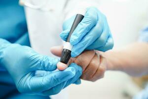Asian doctor using lancet pen on senior patient finger for check sample blood sugar level to treatment diabetes. photo