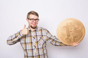 Happy cheerful young man holding big golden bitcoin on white background. Crypto currency, virtual money, internet and economics concept photo