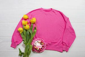 Closeup pink blank template sweatshirt hoodie copy space. Mothers women day yellow tulips, cake. Happy birthday top view mockup pullover. White wooden background. Casual outfit. Flat lay templates photo