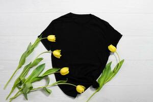 negro camiseta Bosquejo. modelo blanco camisa parte superior vista. blanco de madera antecedentes. madre mujer día día festivo. amarillo tulipanes mujer camiseta con cumpleaños ramo de flores flores primavera mirar. hembra accesorios foto