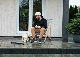 A young man rests near his country house with a dog. photo