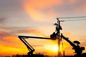 Silhouette of Electrician officer climbs a pole and uses a cable car to maintain a high voltage line system, Shadow of Electrician lineman repairman worker at climbing work on electric post power pole photo