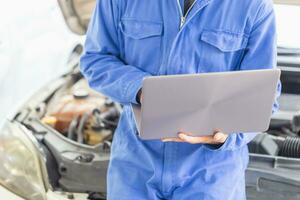 Auto mechanic working on laptop at mechanic shop, technician diagnosing car engine with a laptop with special program photo