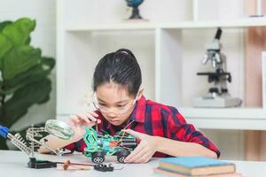 asiático niño niña estudiantes construir robótico carros, niños aprender a programa robot vehículos foto