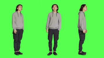 Asian man waving hello at people, greeting someone with a smile and confidence against full body greenscreen template. Young adult saying hi with a wave, smiling and feeling positive in studio. video