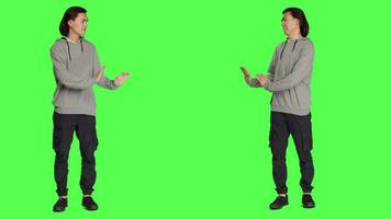 In studio, person tries to shove object aside, presenting rejection or resistance. Against isolated full body greenscreen set, young model resembles refusal and disagreement with stop gesture. video