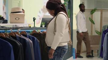 Woman getting interrupted by friend while browsing through wares in thrift shop with vintage clothes. Customer surprised to meet acquaintance in premium second hand clothing store video