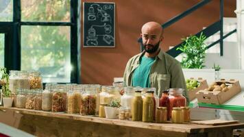 Shop owner presents pasta types to client, opening sustainable containers filled with bulk products in natural eco grocery store. Vendor recommending organic chemicals free food items. video