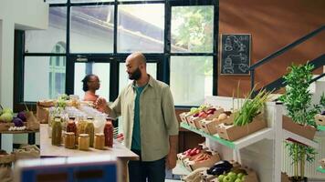 comerciante às Verificação de saída digitalização e ponderação bens para vender para freqüente cliente dentro local zero desperdício eco loja. jovem adulto colocando legumes em escala, vendendo localmente crescido produzir. video