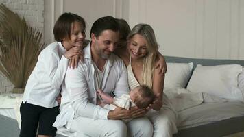 une grand famille est accordé sur une nouveau née enfant séance sur le lit à maison. famille de cinq. video