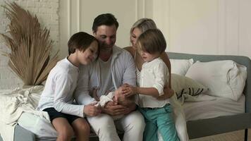 A large family is bestowed upon a newborn child sitting on the bed at home. Family of five. video