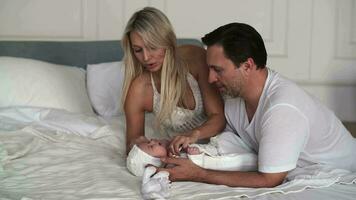 Father and mother dress their newborn baby on the bed in the bedroom. video