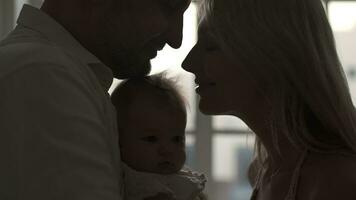 Mom and father are holding a newborn baby in their arms while standing near the window. video